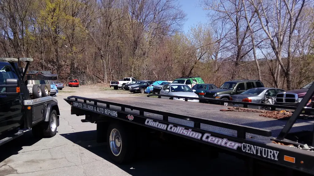 A Guaranty Auto flatbed tow truck bed lettered Clinton Collision Center, lot behind