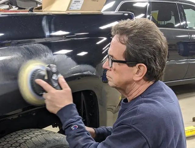 A Guaranty Auto body technician buffing a dark vehicle panel