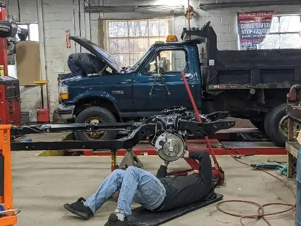 A dump truck up on the frame machine at Guaranty Auto, with a technician working underneath