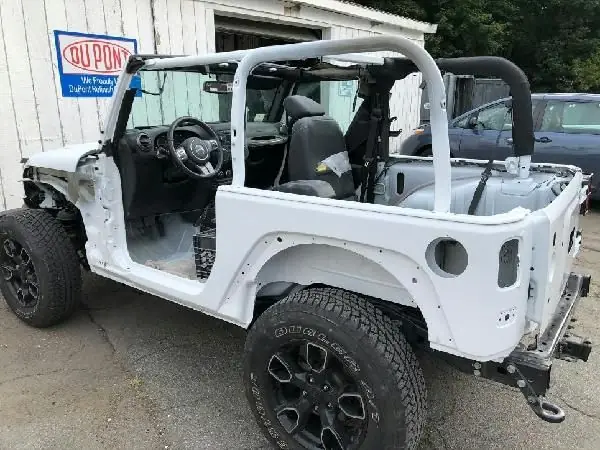 A white Jeep with its body lifted off, under repair inside the Guaranty Auto body shop