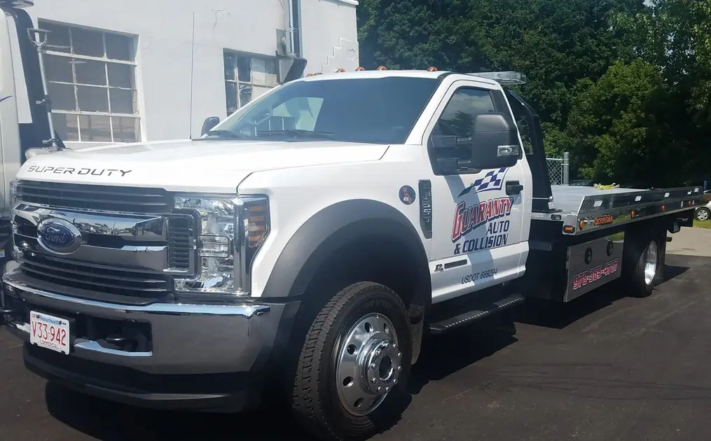 A white Ford Super Duty flatbed tow truck in Guaranty Auto & Collision livery